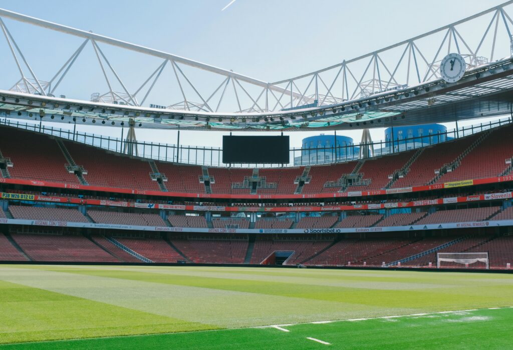 Empty soccer stadium with striking architecture in London, England, showcasing red seating and green pitch.